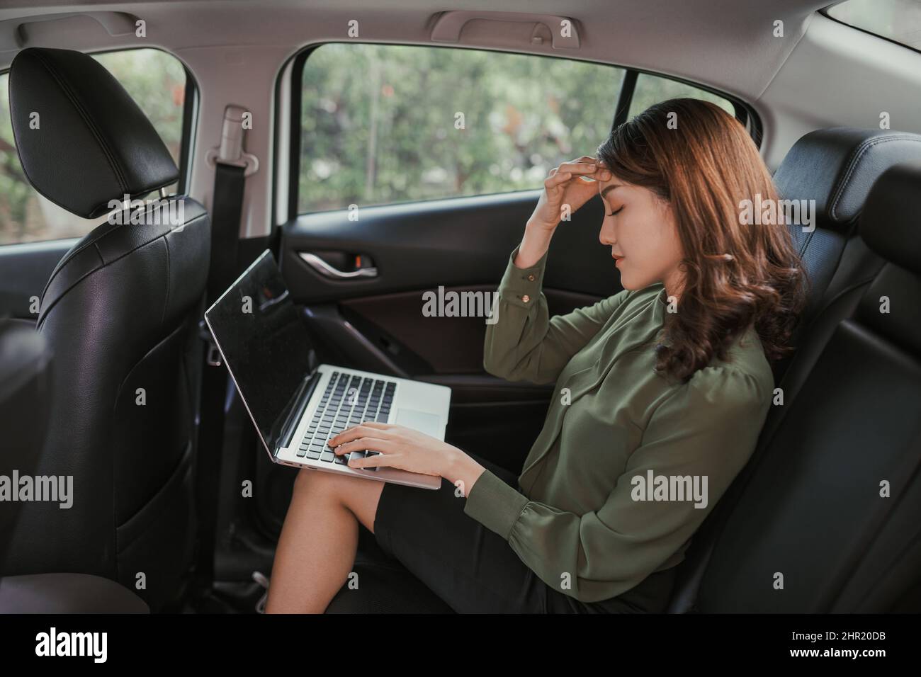 Gestresste junge Geschäftsfrau mit Laptop-Computer, während sie auf dem Rücksitz des Autos sitzt Stockfoto