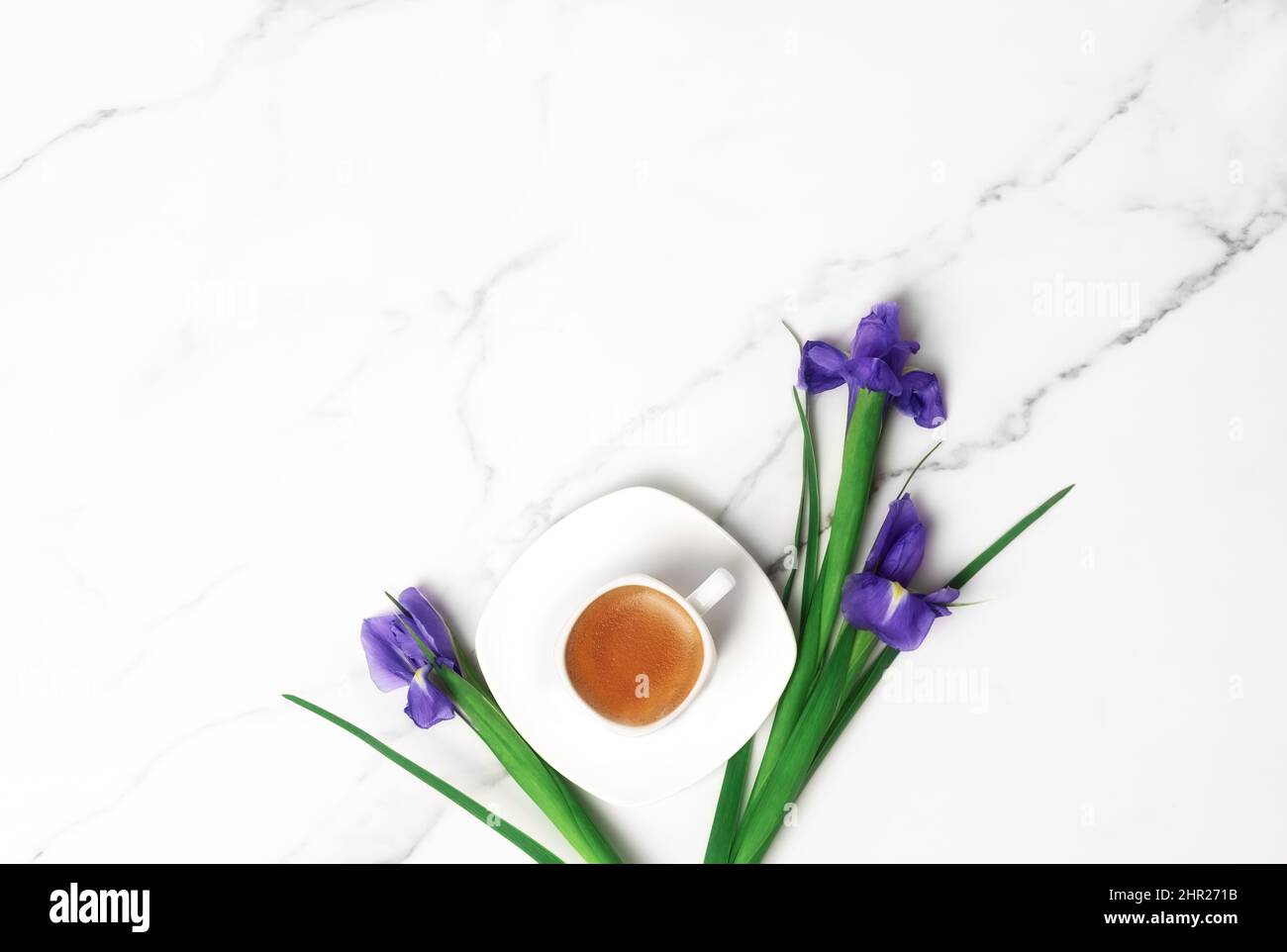 Tasse heißen Morgenkaffee und violette Iris auf Marmorboden. Flach liegend mit Platz für Text. Grußkarte zum Frauentag und 8.. März. Stockfoto