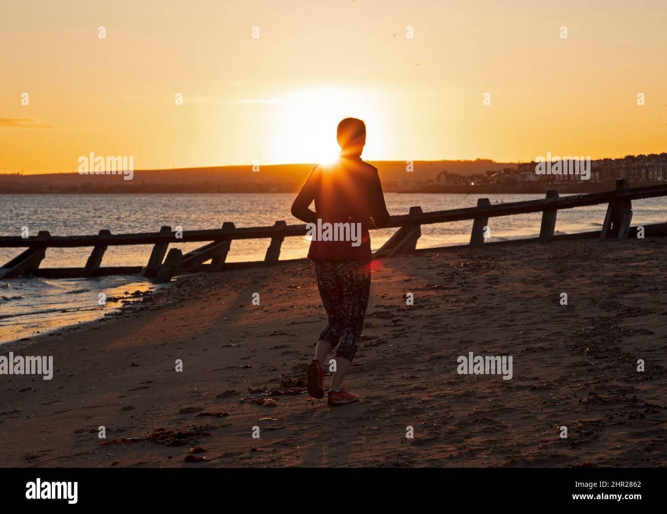 Portobello, Edinburgh, Schottland, Großbritannien. 25.. Februar 2022. Kühler Sonnenaufgang am Meer am Firth of Forth mit einer Temperatur von 2 Grad Celsius für diejenigen, die Sport treiben. Im Bild: Eine Frau joggt entlang der Sandtürme der Strand groynes. Kredit: Archwhite/alamy Live Nachrichten. Stockfoto