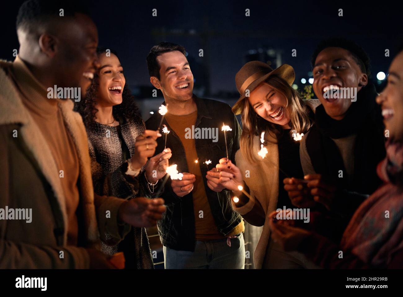 Eine bunte Gruppe von Freunden lachend auf einer Party auf der Dachterrasse. Nachtleben in der Stadt, Beleuchtung Sparklers Stockfoto