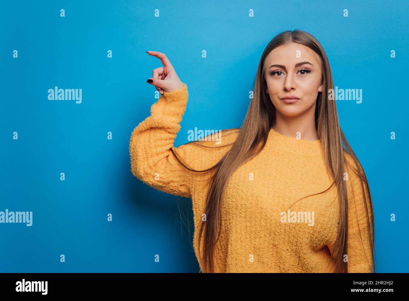 Frau hält etwas mit der Hand und zeigt es der Kamera, während sie auf einem isolierten Hintergrund steht. Stockfoto