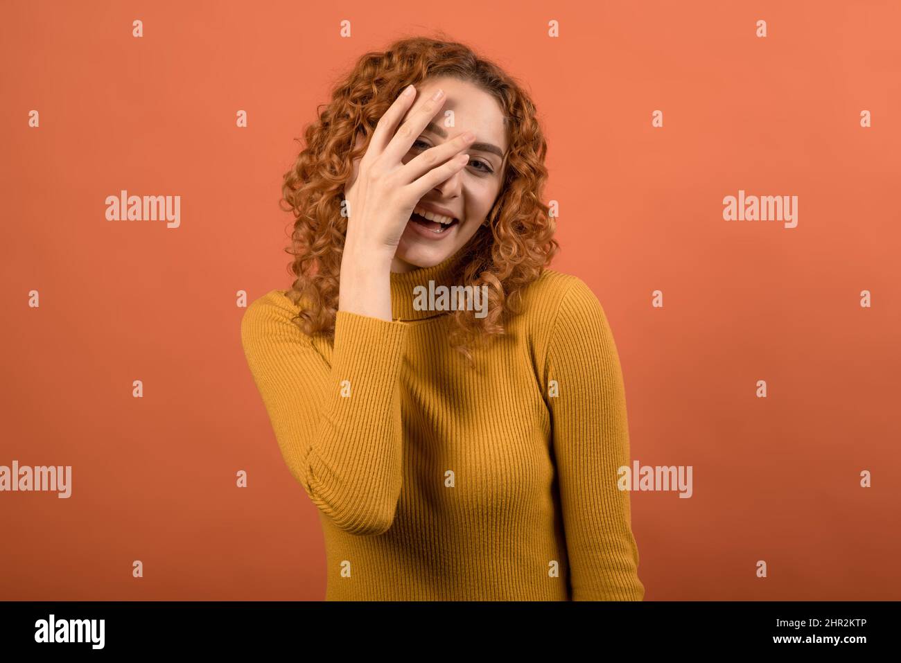 Porträt eines jungen und attraktiven, erfreut und lachend rothaarige kaukasische Mädchen in einem orangefarbenen Jumper isoliert auf einem orangen Studiohintergrund. Stockfoto