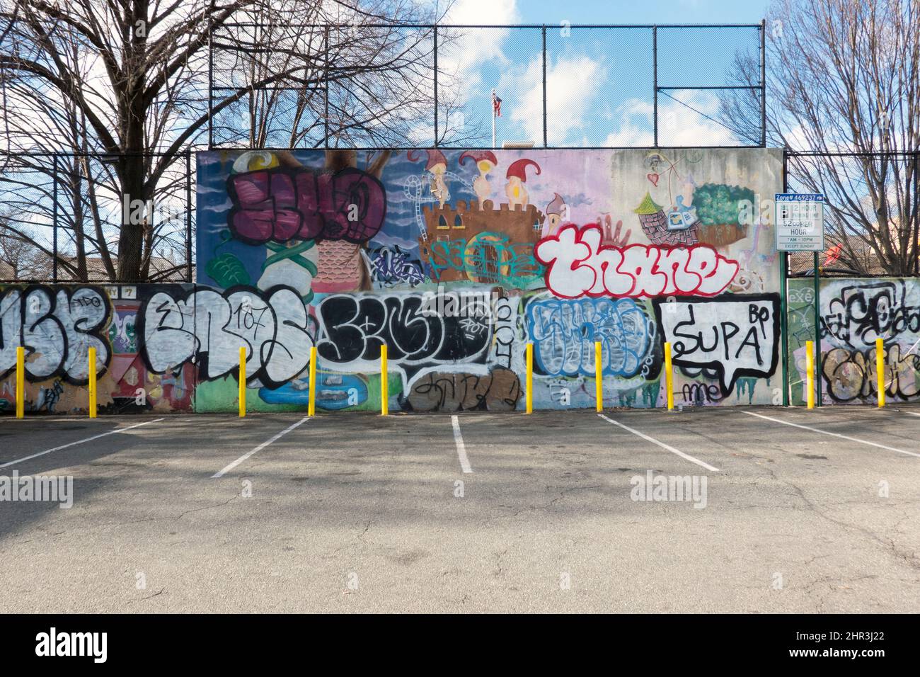 STADTLANDSCHAFT. Ein leerer Parkplatz in der Steinway Street mit einer bemalten Mauer, einem Zaun und einem blauen Himmel. In Astoria, Queens, New York City. Stockfoto