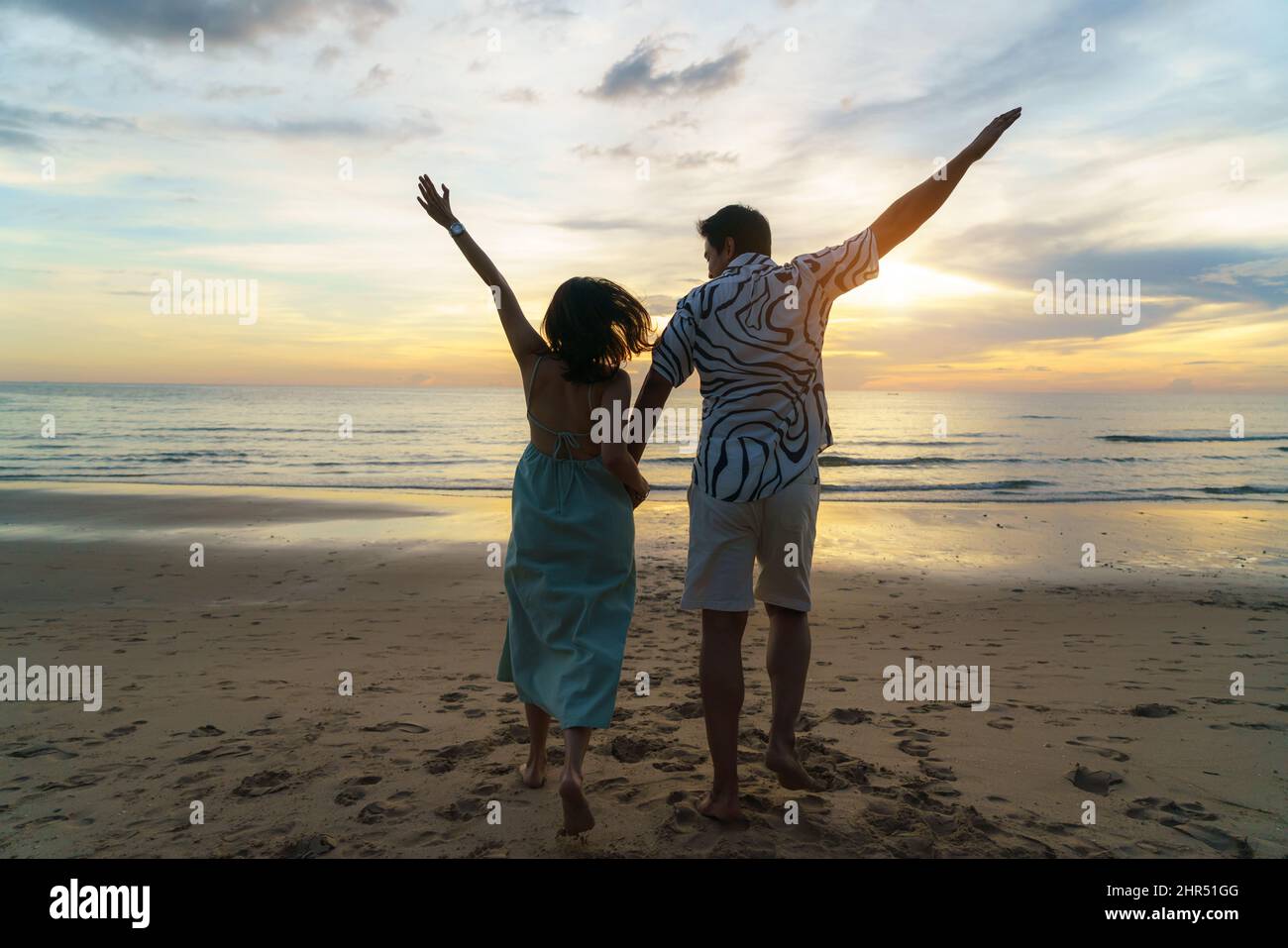 Asiatische Frau Reisende halten Mann die Hand und schauen schönen Sonnenuntergang am Strand, Paar im Urlaub im Sommer und Freiheit Konzept Stockfoto