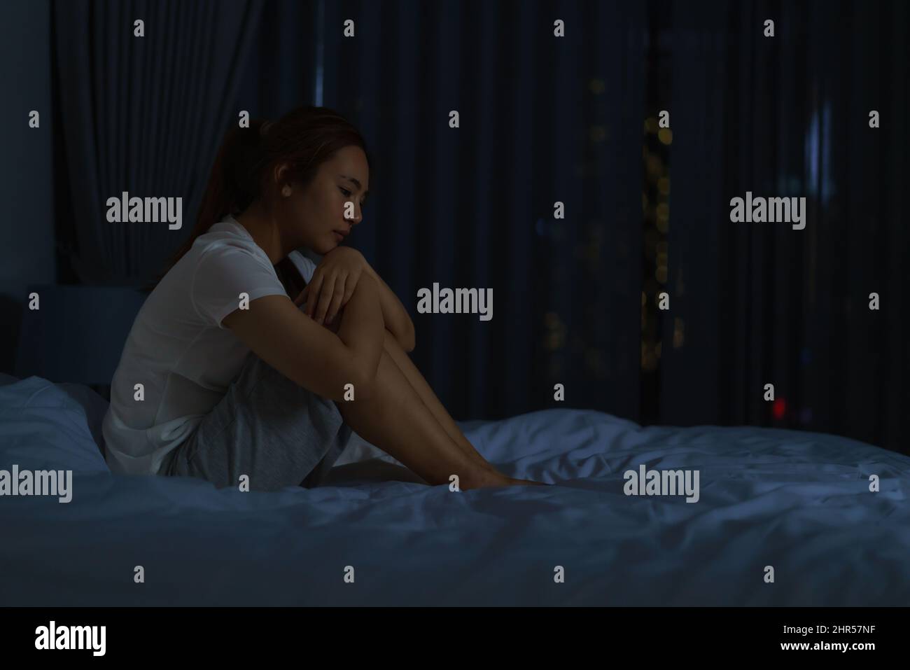Asiatische Frau, die auf einem weißen Bett im Schlafzimmer liegt und besorgt aussieht oder über etwas über ihr Leben oder ihre Arbeit in der Nacht zu Hause nachdenkt. Stockfoto