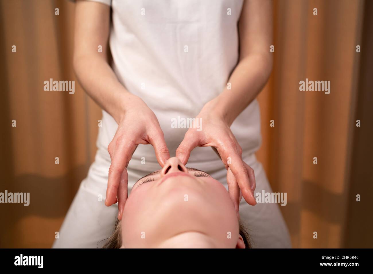 Die Kosmetikerin massiert in einer Kosmetikklinik die Gesichtshaut einer Frau. Die Kosmetikerin beginnt zu massieren. Spa-Behandlungen in einer Schönheit Stockfoto