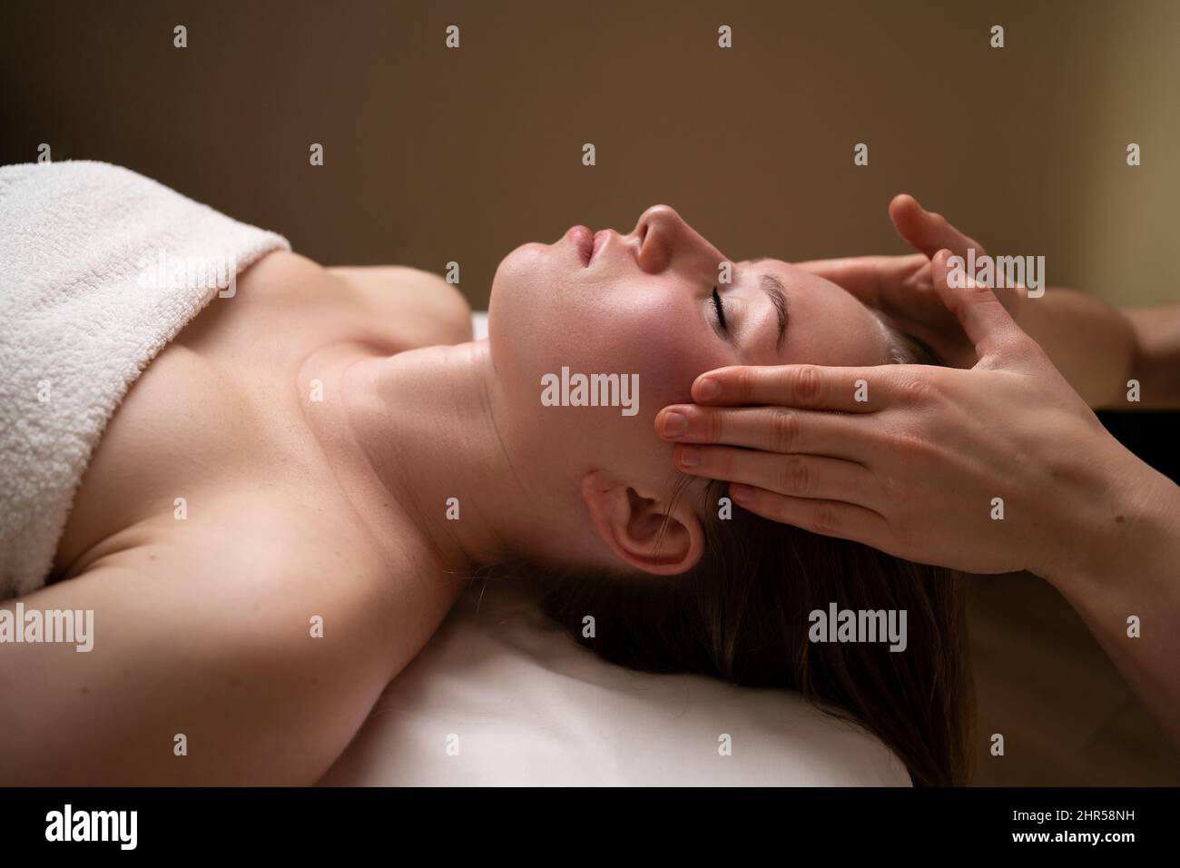 Weibliche Therapeutin massiert das Gesicht und die Stirn eines entspannten Klienten an eine junge Frau. Entspannende Massage. Gesichtsmassage. Alternative Medizin. Stockfoto