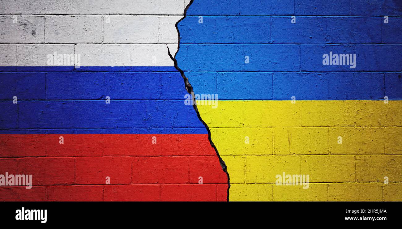 Gesprungene Ziegelwand mit einer russischen Flagge auf der linken Seite und einer ukrainischen Flagge auf der rechten Seite. Stockfoto