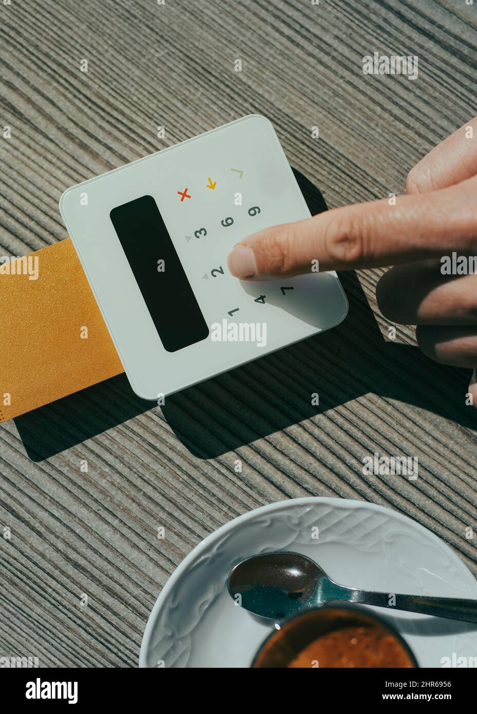 Blick aus der Perspektive eines jungen Mannes, der an einem Tisch eines Straßencafés sitzt, während er den PIN-Code seiner Kreditkarte in das Yepad einer Zahlungs-te einfügt Stockfoto