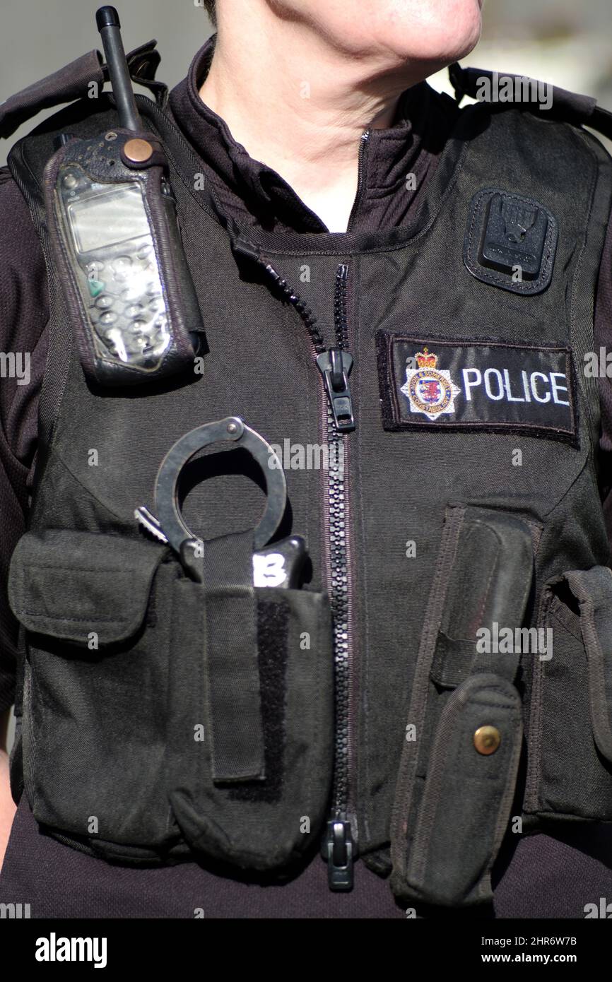 Nahaufnahme einer weiblichen britischen Polizeibeamten mit Körperpanzerung oder Dienstweste, ausgestattet mit Handschellen, persönlichem Radio, Spange und Polizeisignalen Stockfoto