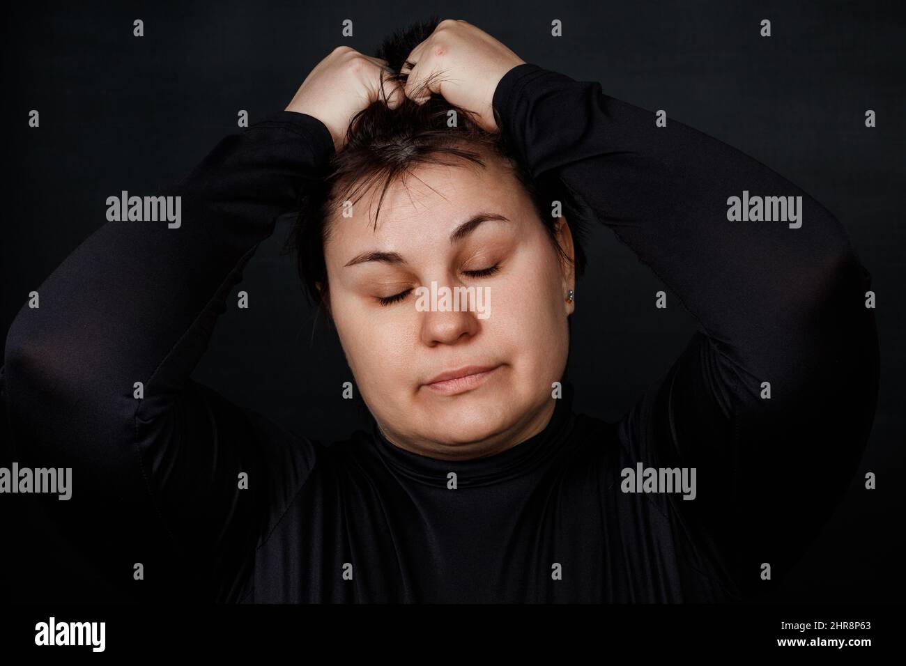 Brünette Frau hält sich an ihrem Kopf und schließt ihre Augen auf einem schwarzen Hintergrund. Hochwertige Fotos Stockfoto