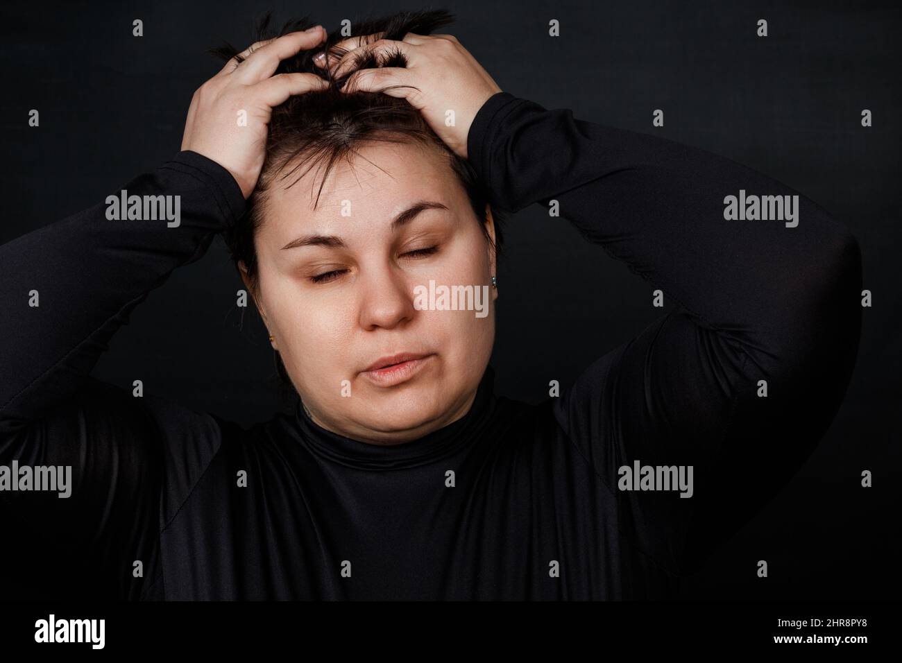 Brünette Frau hält sich an ihrem Kopf und schließt ihre Augen auf einem schwarzen Hintergrund. Hochwertige Fotos Stockfoto