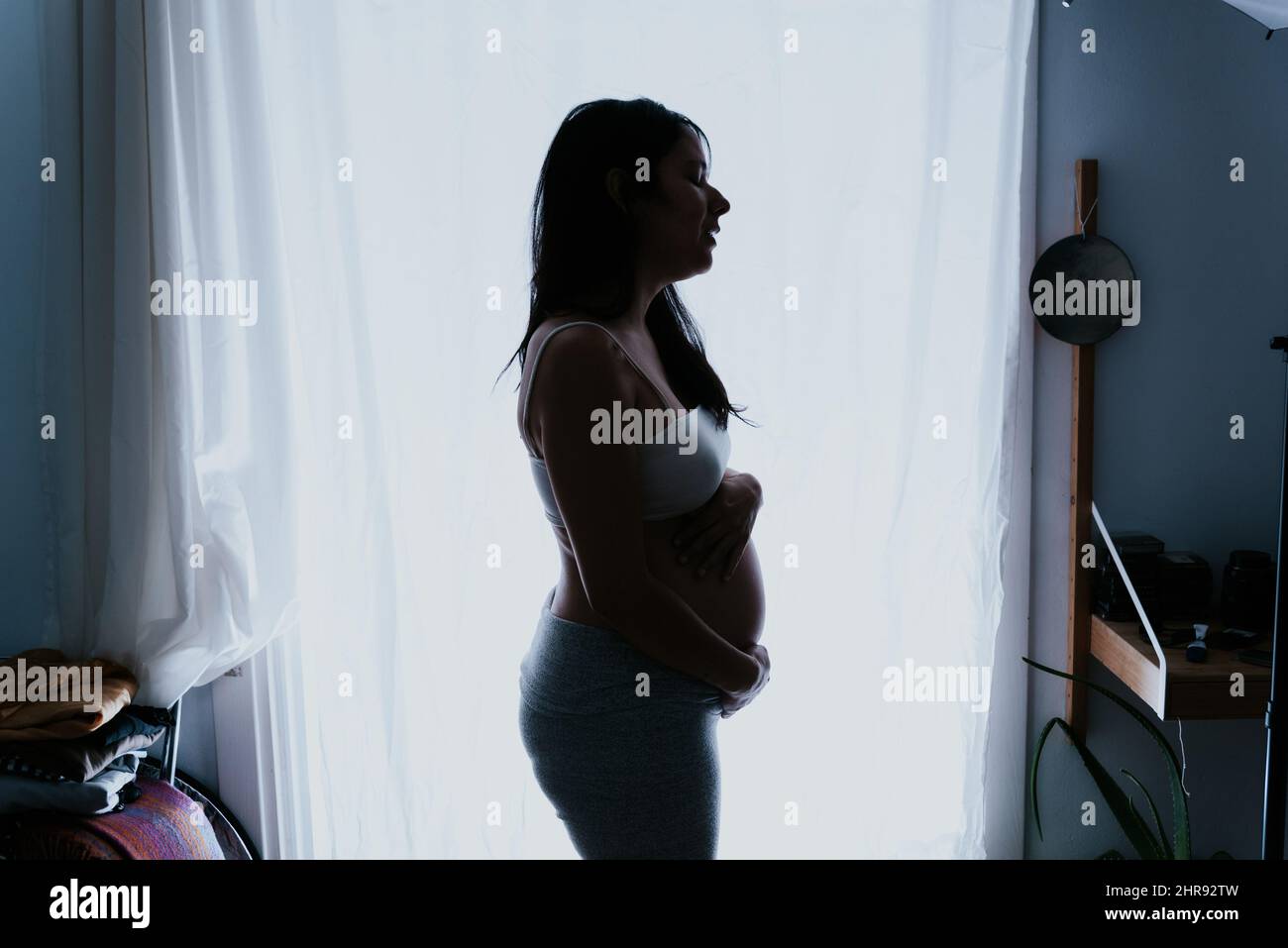 Schwanger Frau Silhouette steht gegen das Fenster. Intime Porträt erwartet Frau berühren ihren großen Bauch. Konzept der Mutterschaft und Mutterschaft Stockfoto