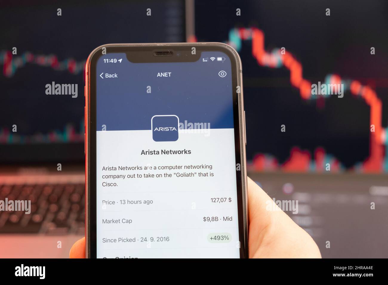 Abwärtstrend der Aktienkursen von Arista Networks mit roten Grafiken im Hintergrund. Man hands Holding a Smartphone with Logo on the screen, February 2022, San Francisco, USA. Stockfoto