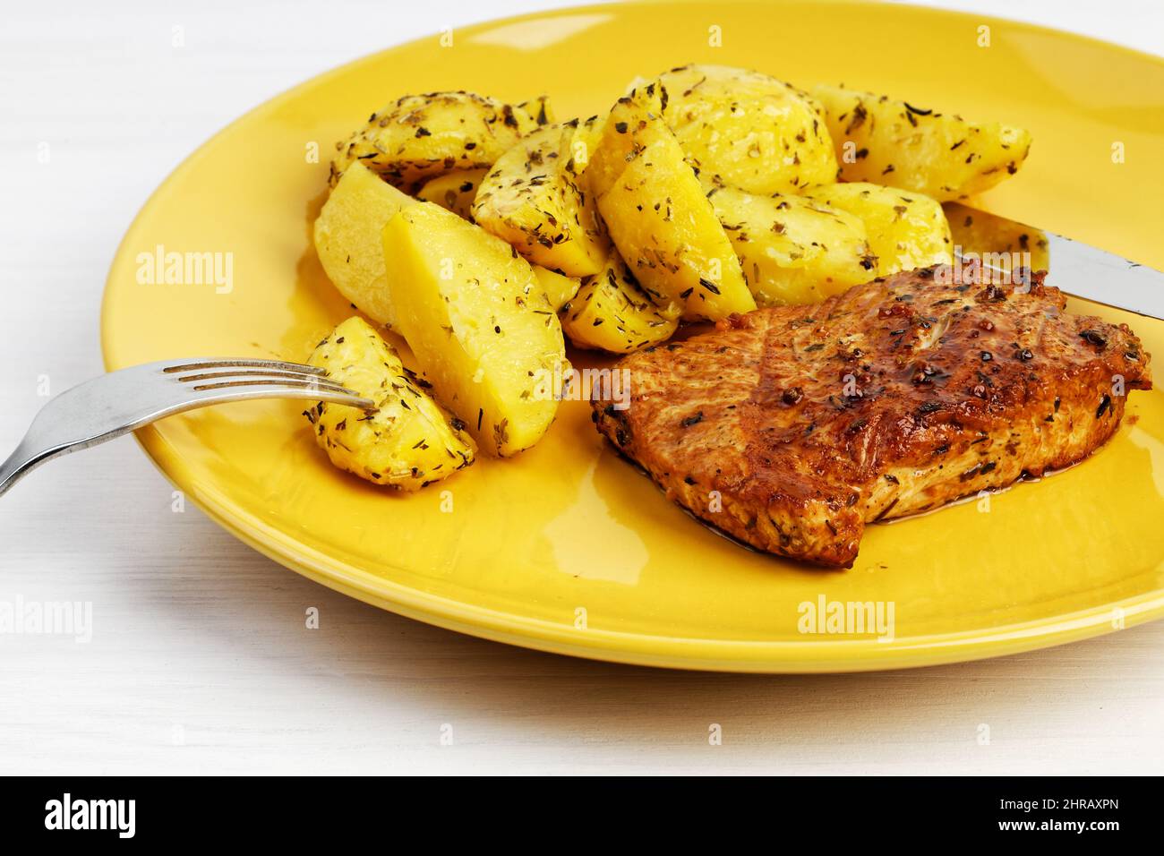 Nahaufnahme gegrilltes putensteak mit einer Garnierung von gebackenen Kartoffeln auf einem gelben Teller auf einem weißen Holztisch. Stockfoto