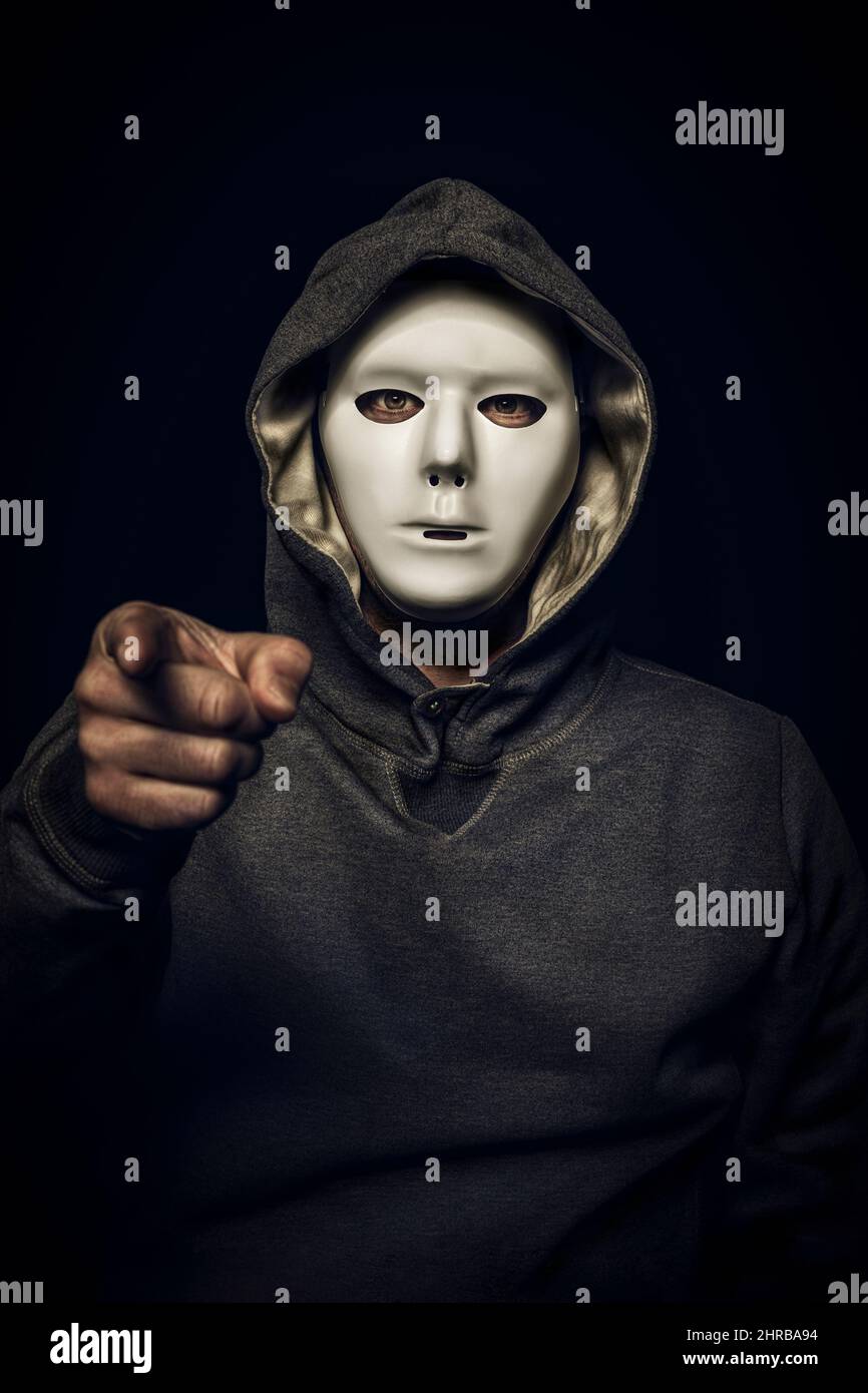 Hacker mit weißer Maske, die Hand zeigt auf die Kamera. Stockfoto