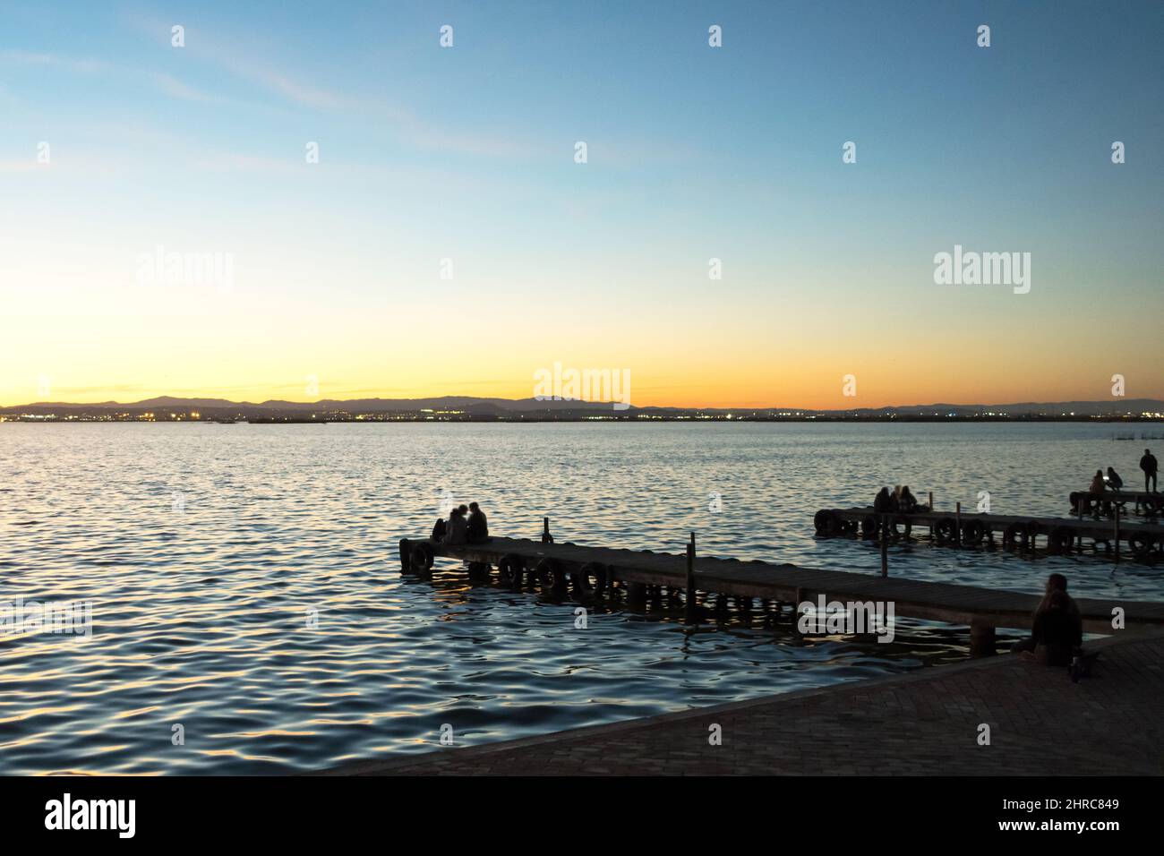 Silhouette von Menschen, die bei Sonnenuntergang auf einem Steg sitzen, Turia River, Albufera, Valencia, Spanien Stockfoto