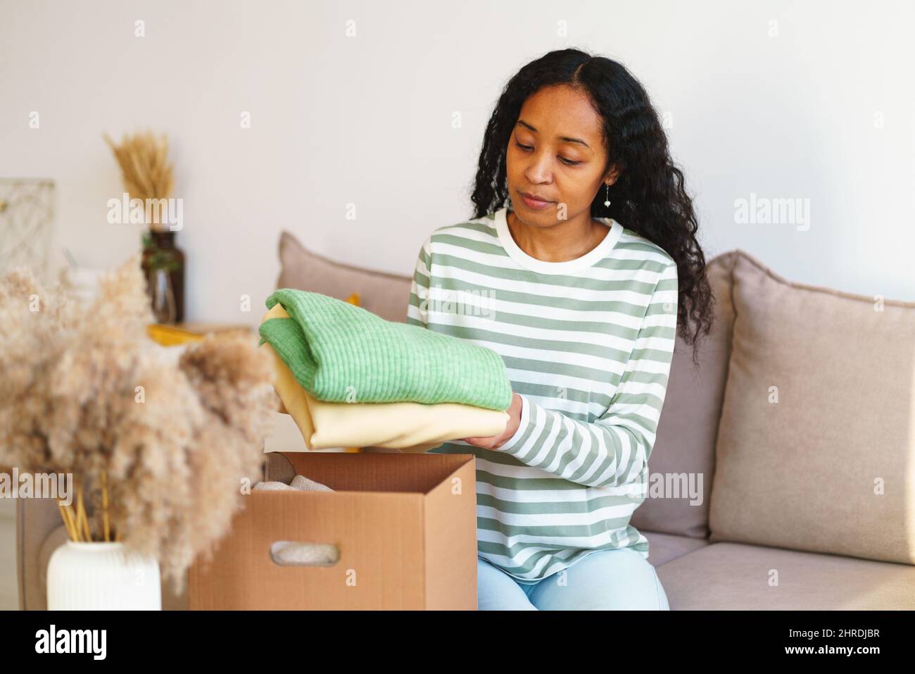 afroamerikanische Frau, die im Wohnzimmer Kleidung für wohltätige Spenden in einen Karton verpackt Stockfoto