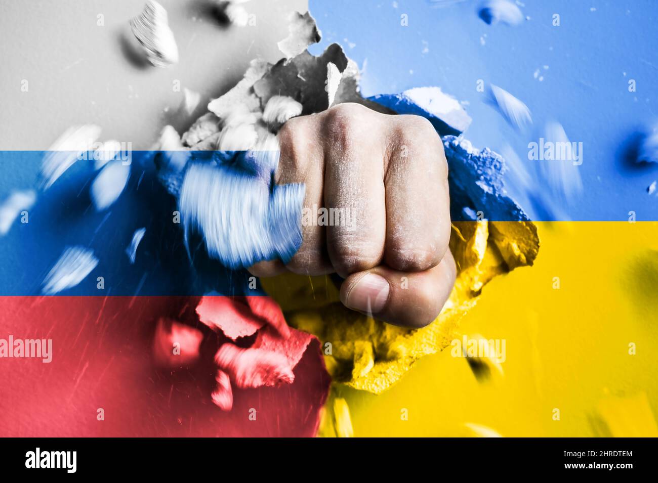 Eine Faust stanzt durch eine Betonwand mit den Farben der ukrainischen und russischen Flaggen. Das Konzept der russischen Aggression gegen die Ukraine Stockfoto