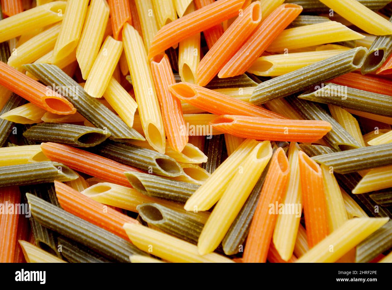 Nahaufnahme von rohen zylinderförmigen Penne Pasta Nudeln in drei Farben Gelb, Grün und Rot Stockfoto