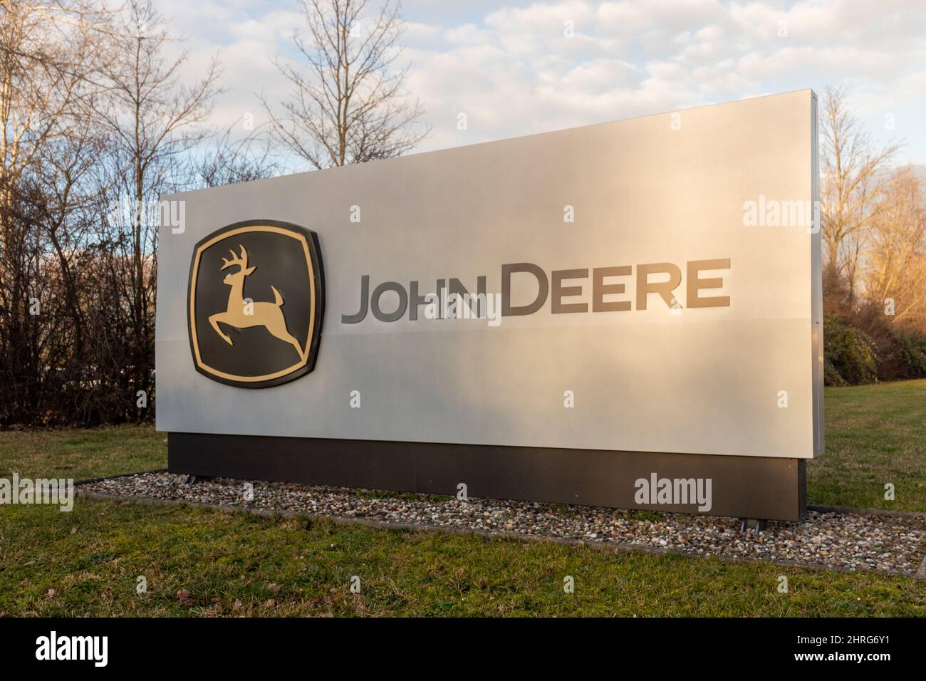 Firmenzeichen von John Deere in Bruchsal, Deutschland. Blauer Himmel mit Wolken und niedriger Sonne Stockfoto