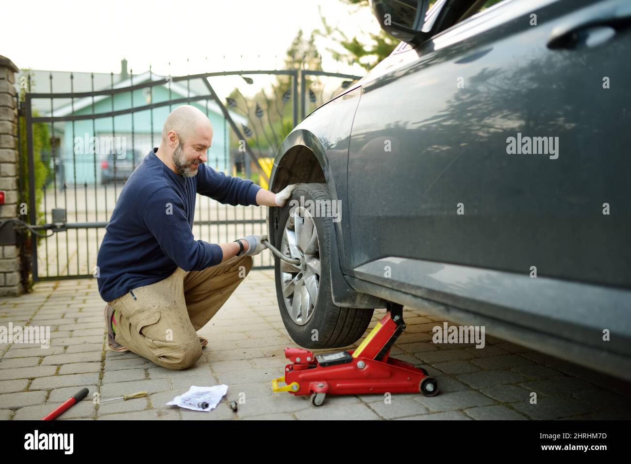 Junger Mann, der die Reifenpanne seines Autos wechselt. Vor dem Aufbocken des Fahrzeugs die Muttern mit einem Radschlüssel lösen. Stockfoto