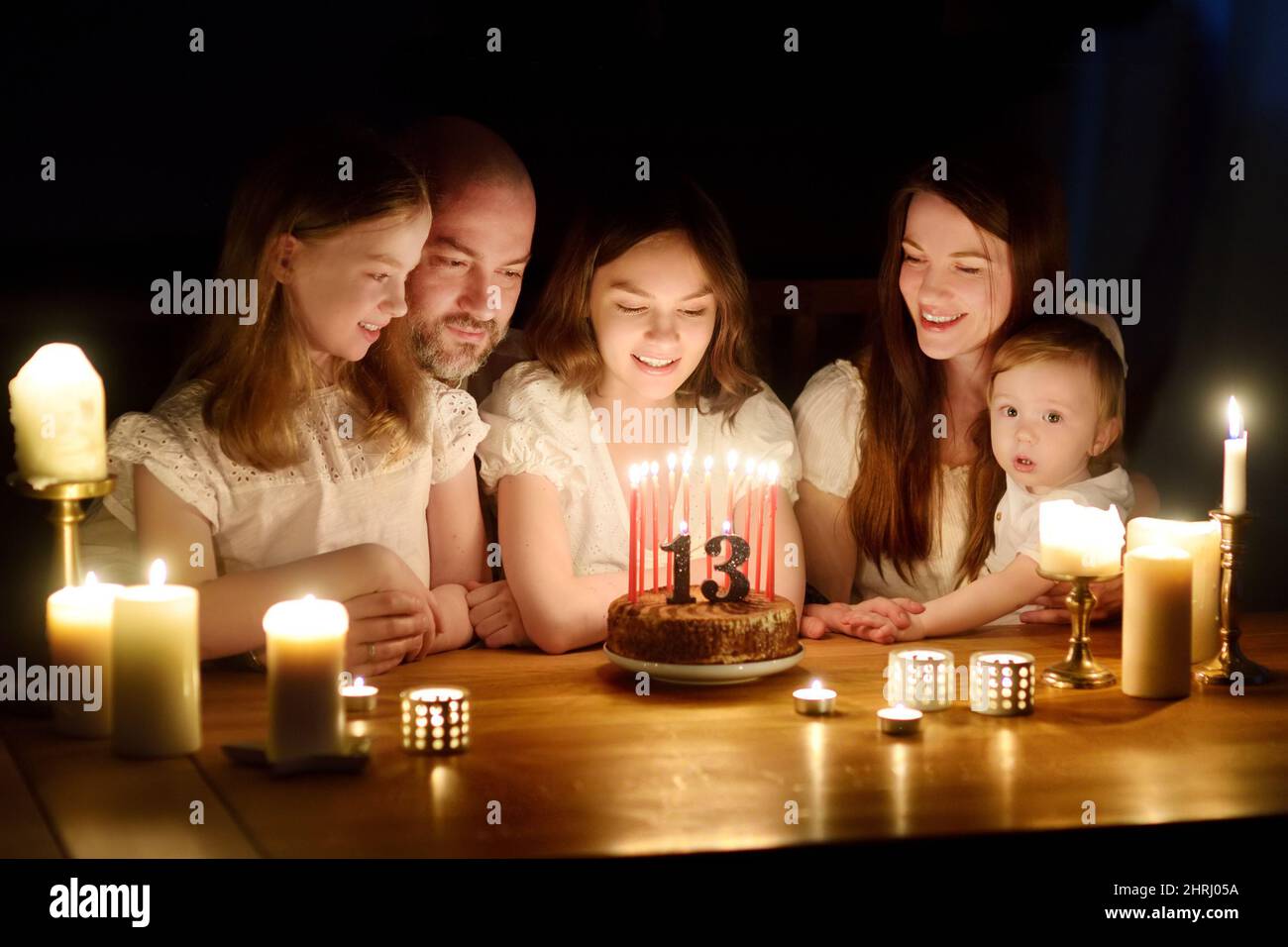 Nettes dreizehn Jahre altes Mädchen, das einen Wunsch macht, bevor es Kerzen auf ihren Geburtstagskuchen bläst. Fünfköpfige Familie feiert Geburtstag von Kindern. Geburtstagstradition Stockfoto