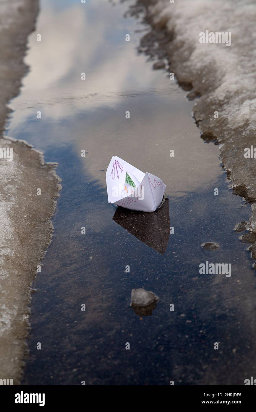 Ein bemaltes Papierboot schwimmt in einer Pfütze aus geschmolzenem Schnee Stockfoto