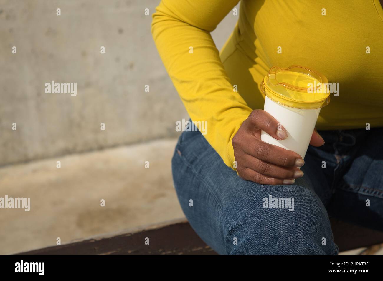 Nahaufnahme einer afroamerikanischen Frau, die eine Tasse Kaffee in der Hand hält und ein gelbes T-Shirt trägt Stockfoto