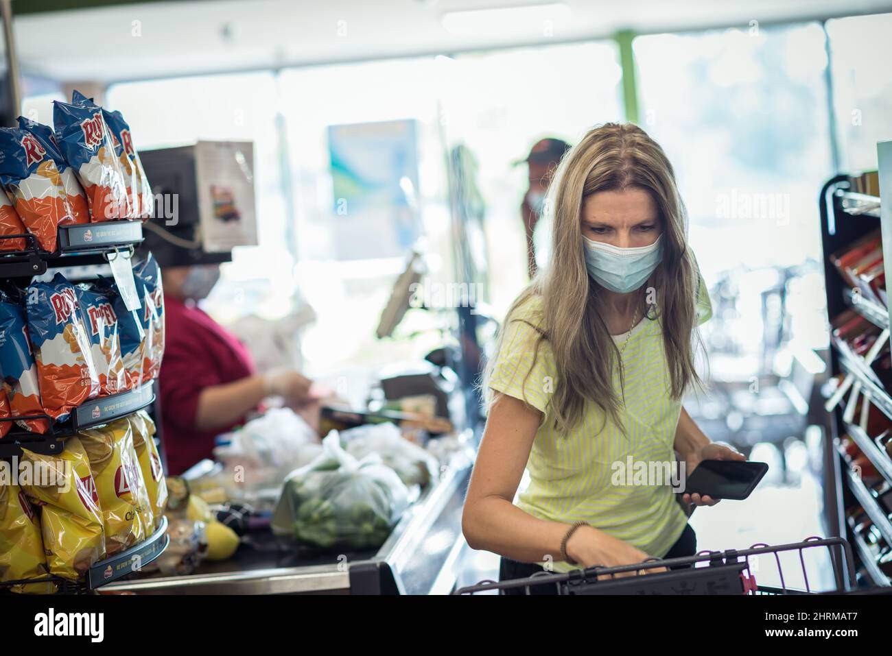 Chicago, IL, 21. August 2021 Eine Frau mit Gesichtsmaske, die Lebensmittel auf das Kassierförderband im Lebensmittelgeschäft lad. Illustratives Editorial. Für ed Stockfoto