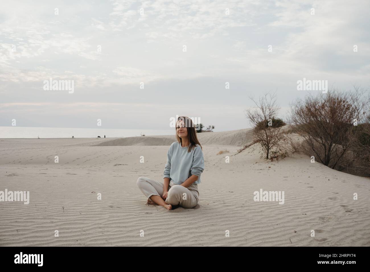 Frau, die auf Sanddünen sitzt, genießt die Aussicht Stockfoto