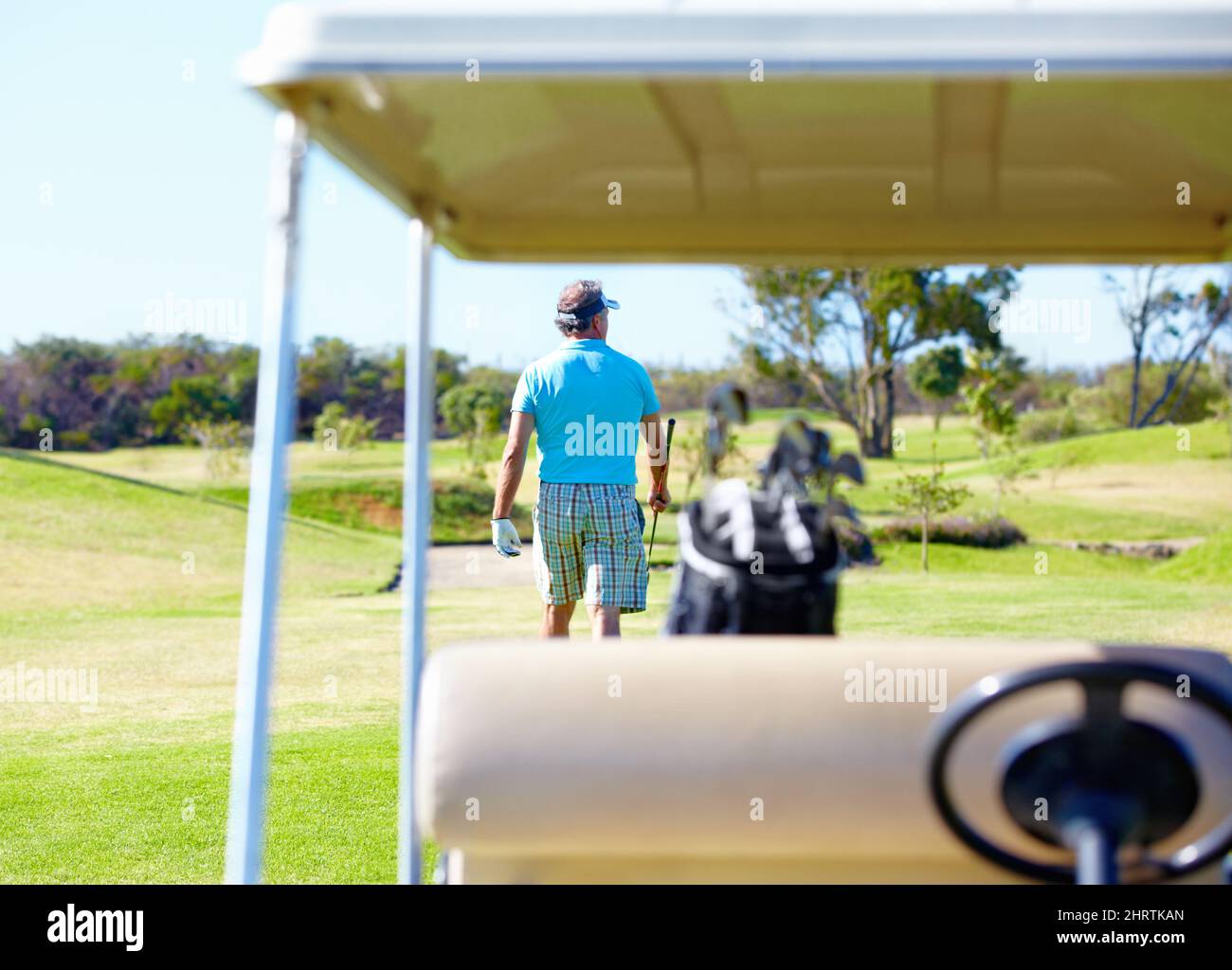 Was für ein toller Tag auf dem Golfplatz zu sein Rückansicht eines Golfspielers, der mit einem Golfwagen im Vordergrund wegläuft. Stockfoto
