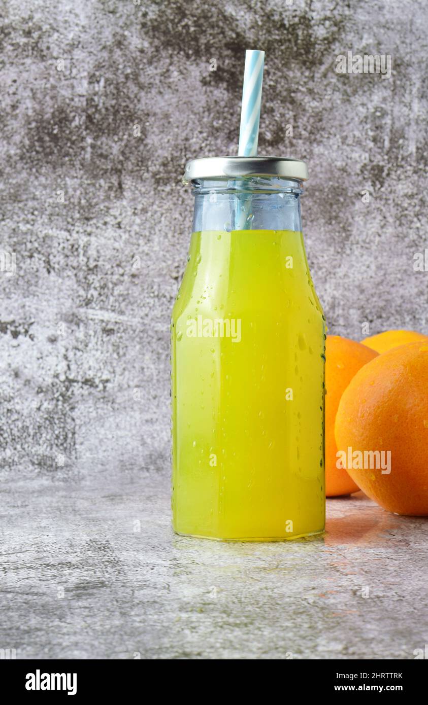 Glasflasche mit erfrischender Orangeade, Steinsockel in hellen Farben Stockfoto