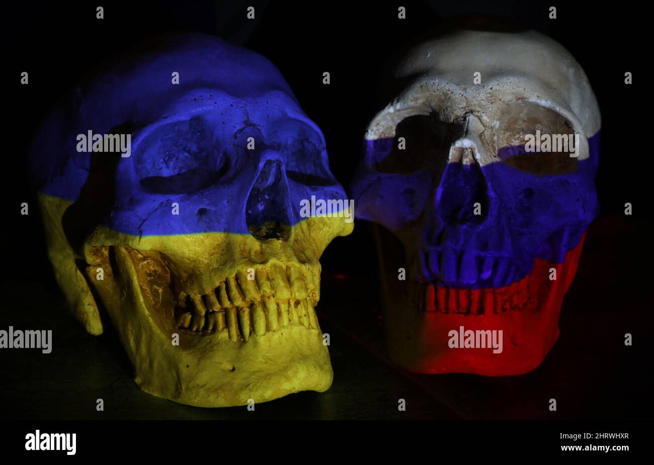 Zwei gegenüberliegende Schädel, die mit den Nationalflaggen Russlands und der Ukraine auf einer abgedunkelten Karte der Region und einem schwarzen Hintergrund bemalt sind. Die w Stockfoto
