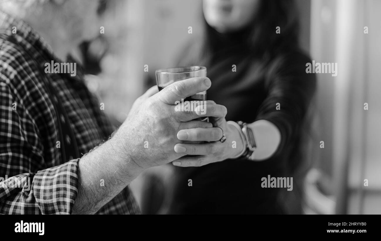 kaukasischer älterer Mann, der Wein trinkt und zu Hause betrunken wird, betont jüngere hispanische Frau - Alkoholismus und häusliche Gewalt Konzept Stockfoto