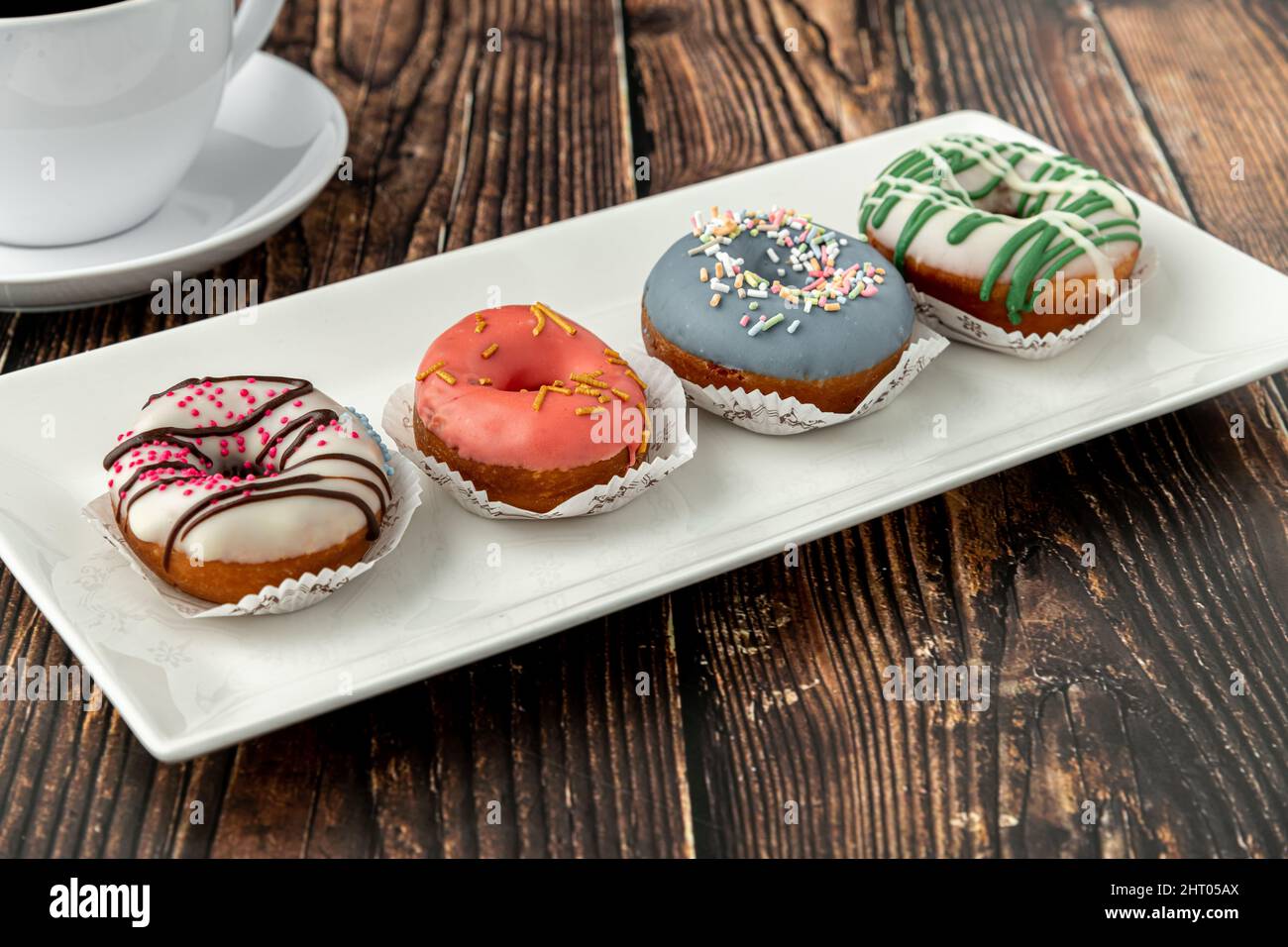 Leckere bunte Mini-Donuts mit Kaffee auf Holztisch Stockfoto