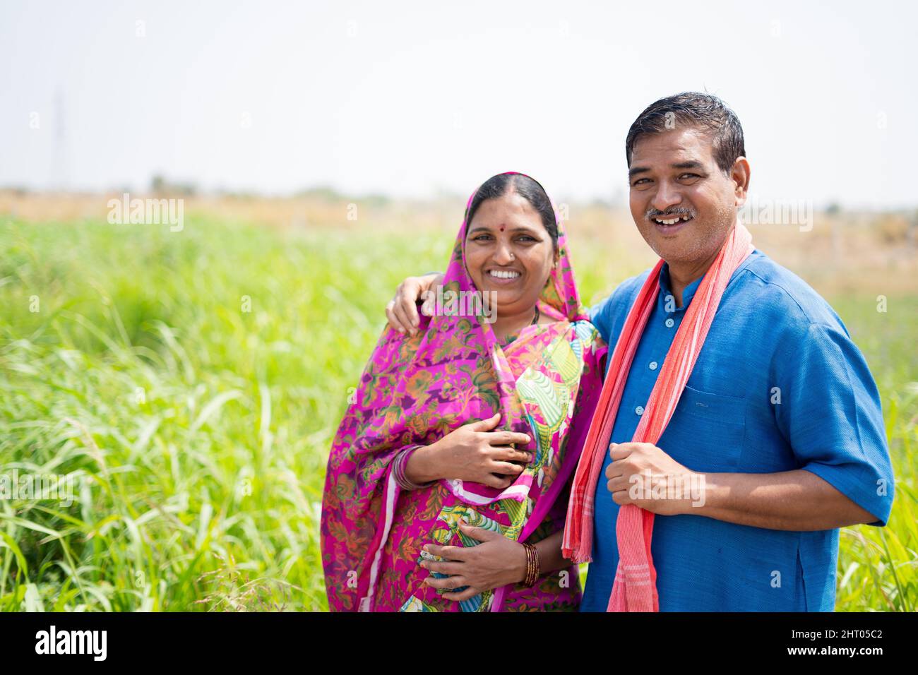 Porträtaufnahme eines lächelnden indischen Dorfpaares auf der Wiese mit Blick auf die Kamera - Konzept von glücklicher Familie, ländlichem Lebensstil und Zweisamkeit Stockfoto