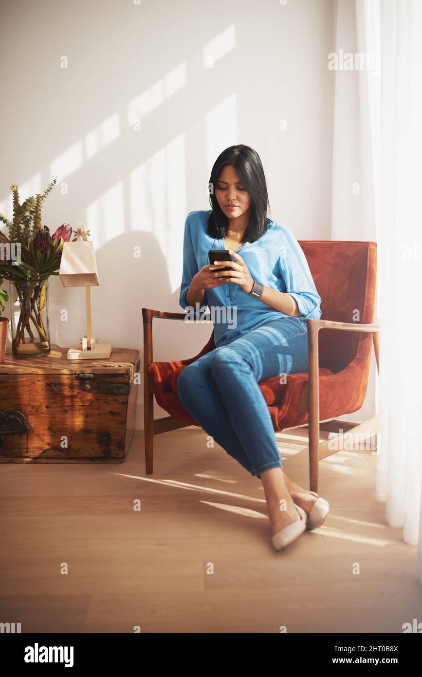 Bleiben Sie auch von zu Hause aus in Verbindung. Aufnahme einer Frau, die ihr Handy benutzt, während sie zu Hause sitzt. Stockfoto