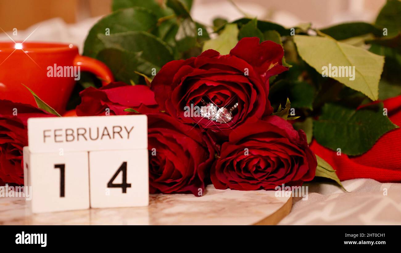 Hintergrund Festliches Flatlay, Komposition zum Valentinstag am 14. Februar. Kaffee in einer roten Tasse, rote Rosenblüten und Diamantherz-Ohrringe zu Hause im Bett Stockfoto