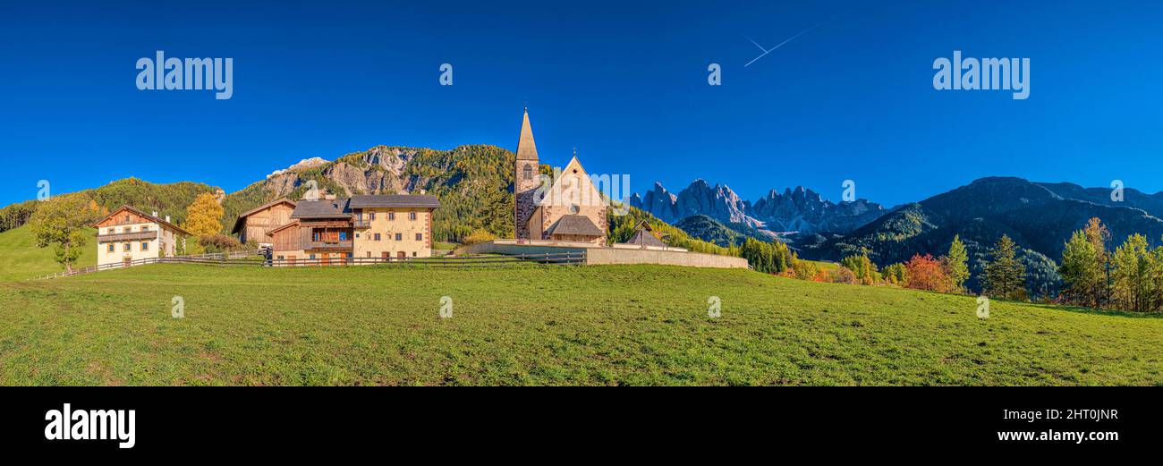 Panoramablick auf die Kirche St. Magdalena im Villnösstal, Nordwände und Gipfel der Geisler-Gruppe in der Ferne, im Herbst. Stockfoto
