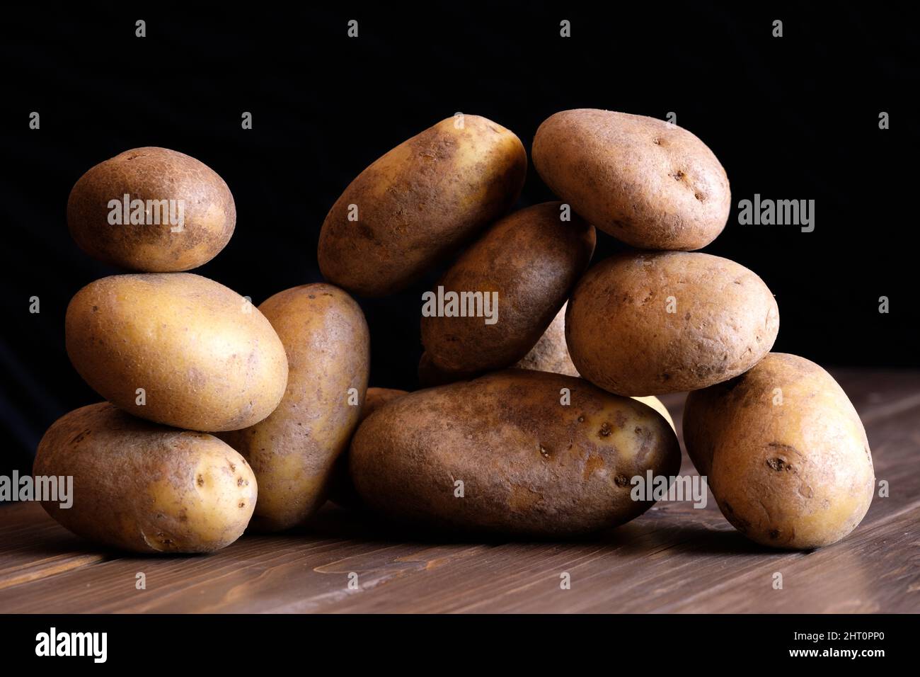 Viele Kartoffeln im Gleichgewicht rohe vegane Lebensmittel Stillleben Chiaroscuro, Gemüse über rustikalen Holzboden schwarz dunklen Hintergrund Stockfoto