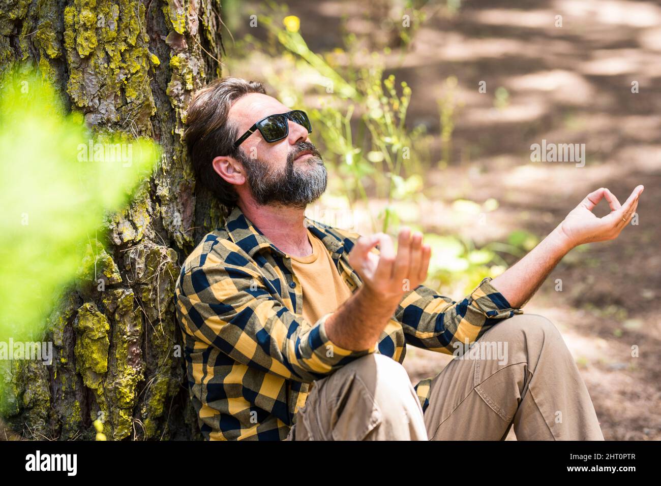 Erwachsene Hipster bärtiger Mann meditieren und entspannen sich im Freien Freizeitaktivitäten in den Wäldern sitzen an einem Baumstamm und genießen Natur fühlen Stockfoto