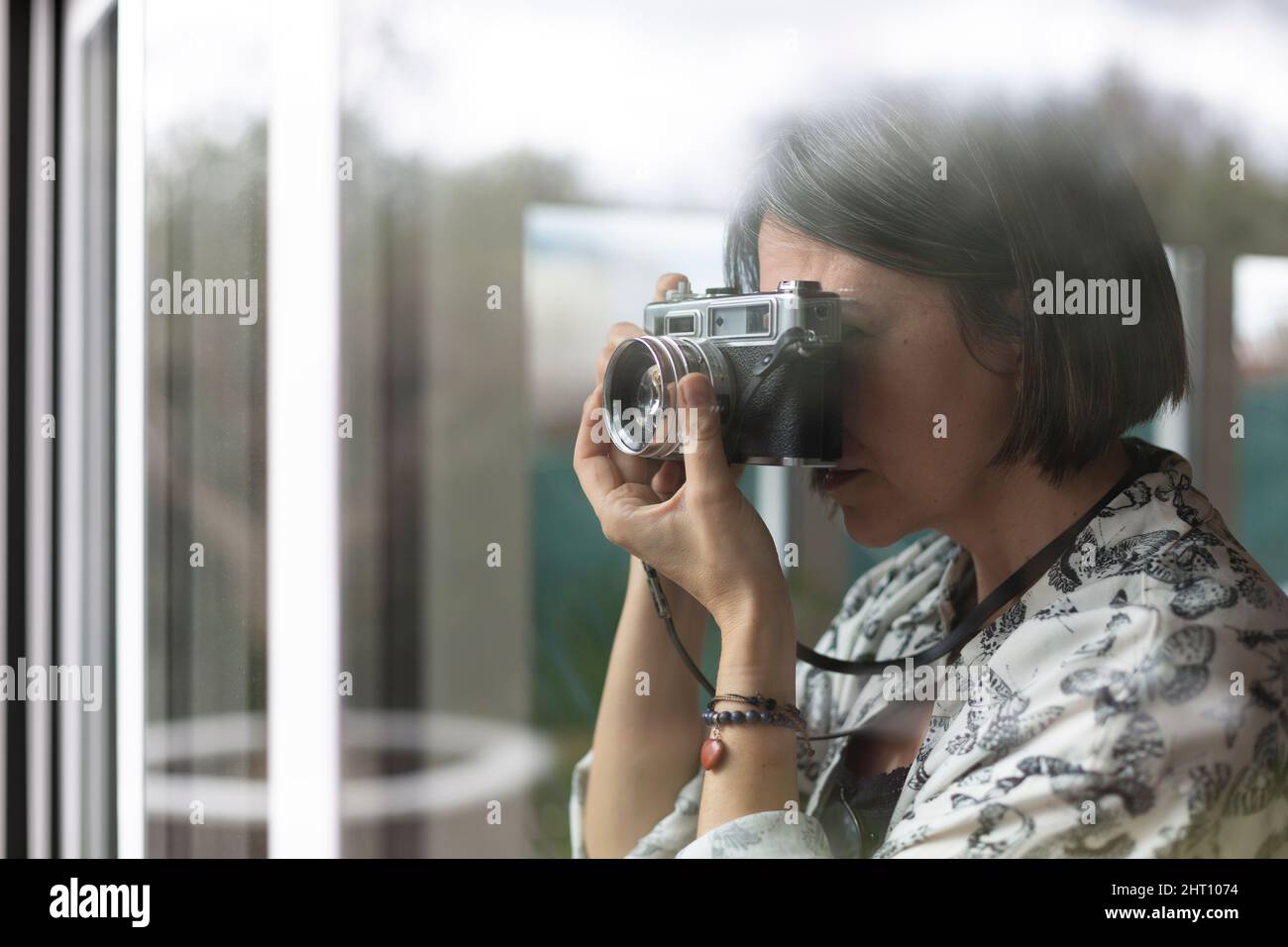 Erwachsene Frau, die mit einer Filmkamera aus dem Fenster ihres Hauses fotografiert. Platz für Text. Stockfoto