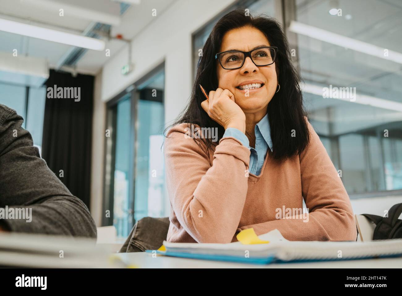 Oberflächennahe Ansicht einer lächelnden, reifen Schülerin, die im Klassenzimmer am Schreibtisch sitzt Stockfoto
