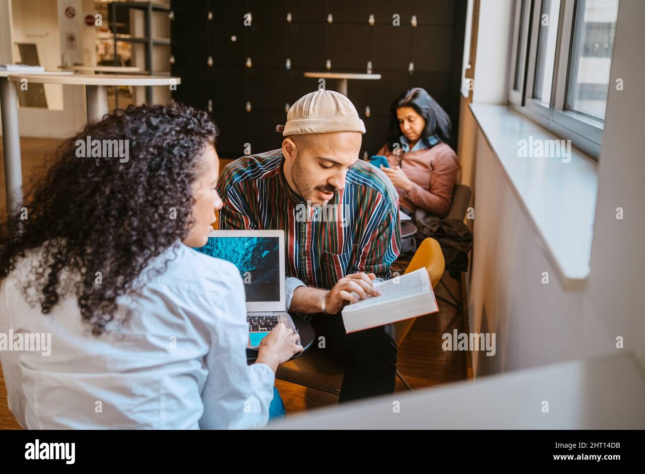 Männliche und weibliche Universitätsstudenten diskutieren über Buch, während sie zusammen studieren Stockfoto