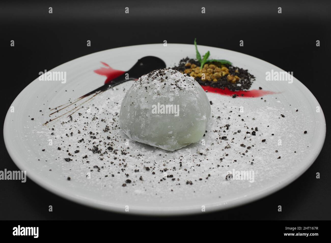 Ein traditionelles japanisches Dessert Mochi mit Schokoladensorbet, Gelatine aus Reis in einem verzierten Teller mit Zuckerpulver auf schwarzem Hintergrund. Stockfoto