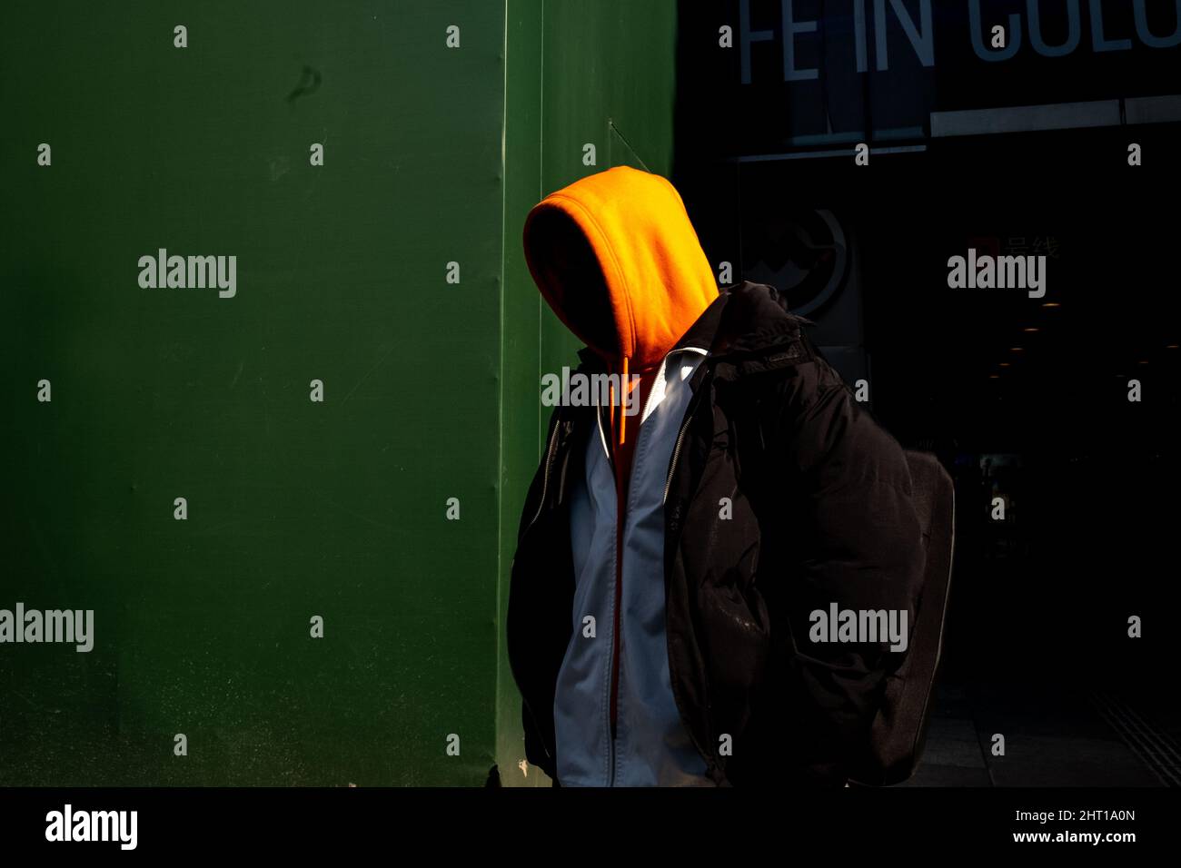 Wunderschöne Aufnahme eines Mannes mit orangefarbenem Hoodie vor einer grünen Wand Stockfoto