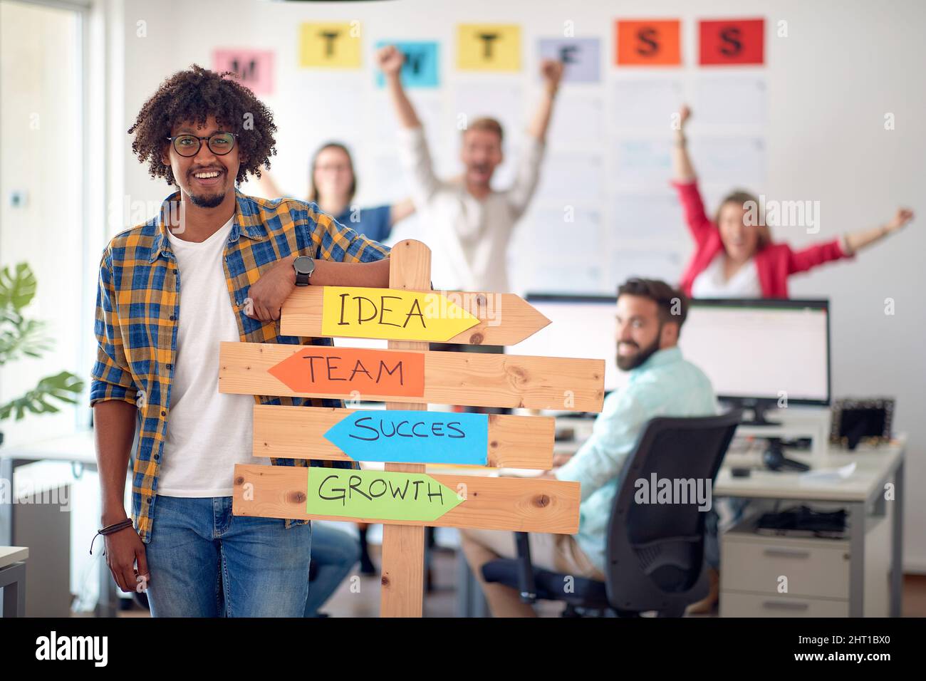 Ein junger Büroangestellter, der in einer angenehmen Atmosphäre im Büro für ein Foto posiert und gleichzeitig ein Schild mit Firmenslogans in der Hand hält. Mitarbeiter, Job, Büro Stockfoto