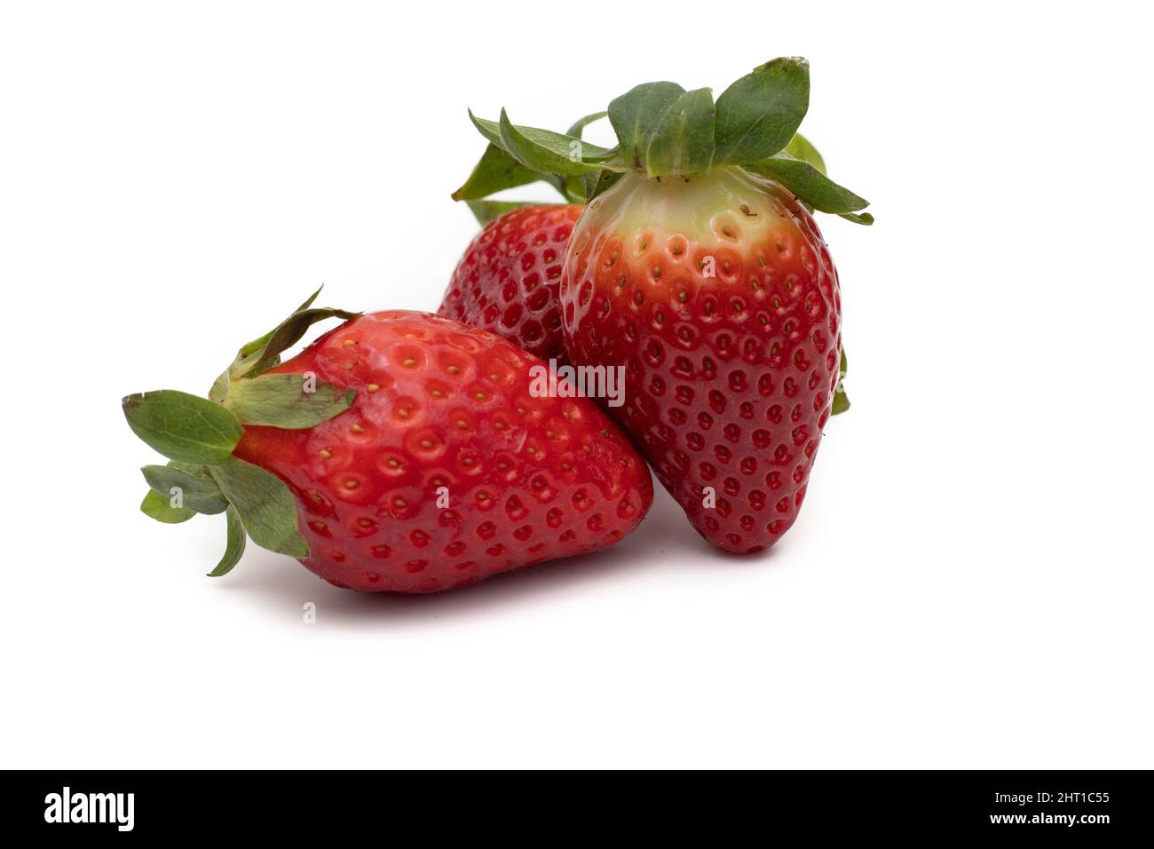 Drei ganze Erdbeeren mit ihren grünen Blättern isoliert auf weißem Hintergrund. Stockfoto