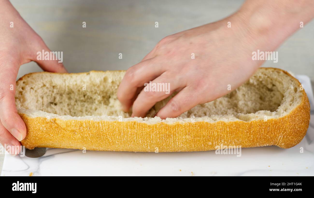 Der Koch schneidet frisches Ciabatta-Brot. Zieht das Fruchtfleisch von innen heraus. Bildet eine Basis für das Füllen von Brot. Riesige Sandwich-Prozess. Stockfoto